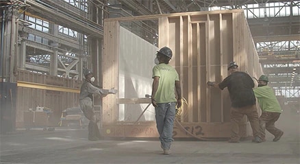 Four men working on a modular building in a dusty construction facility