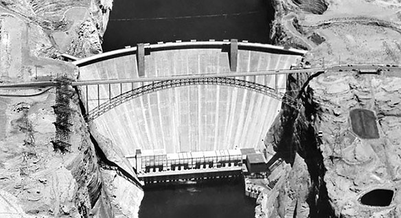 Black-and-white aerial view of a concrete dam set in a rock canyon