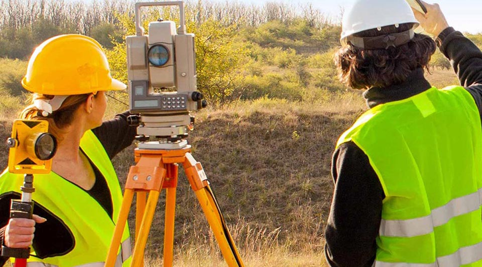 Two engineers use their equipment to survey land at a job site.